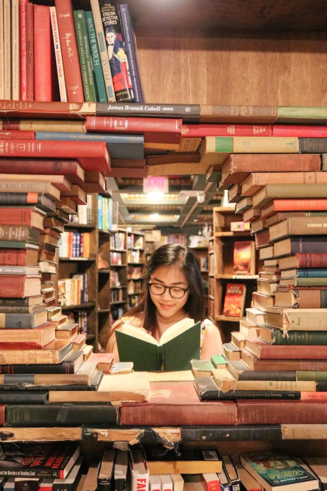 Photo by Ying Ge woman in green shirt sitting on books